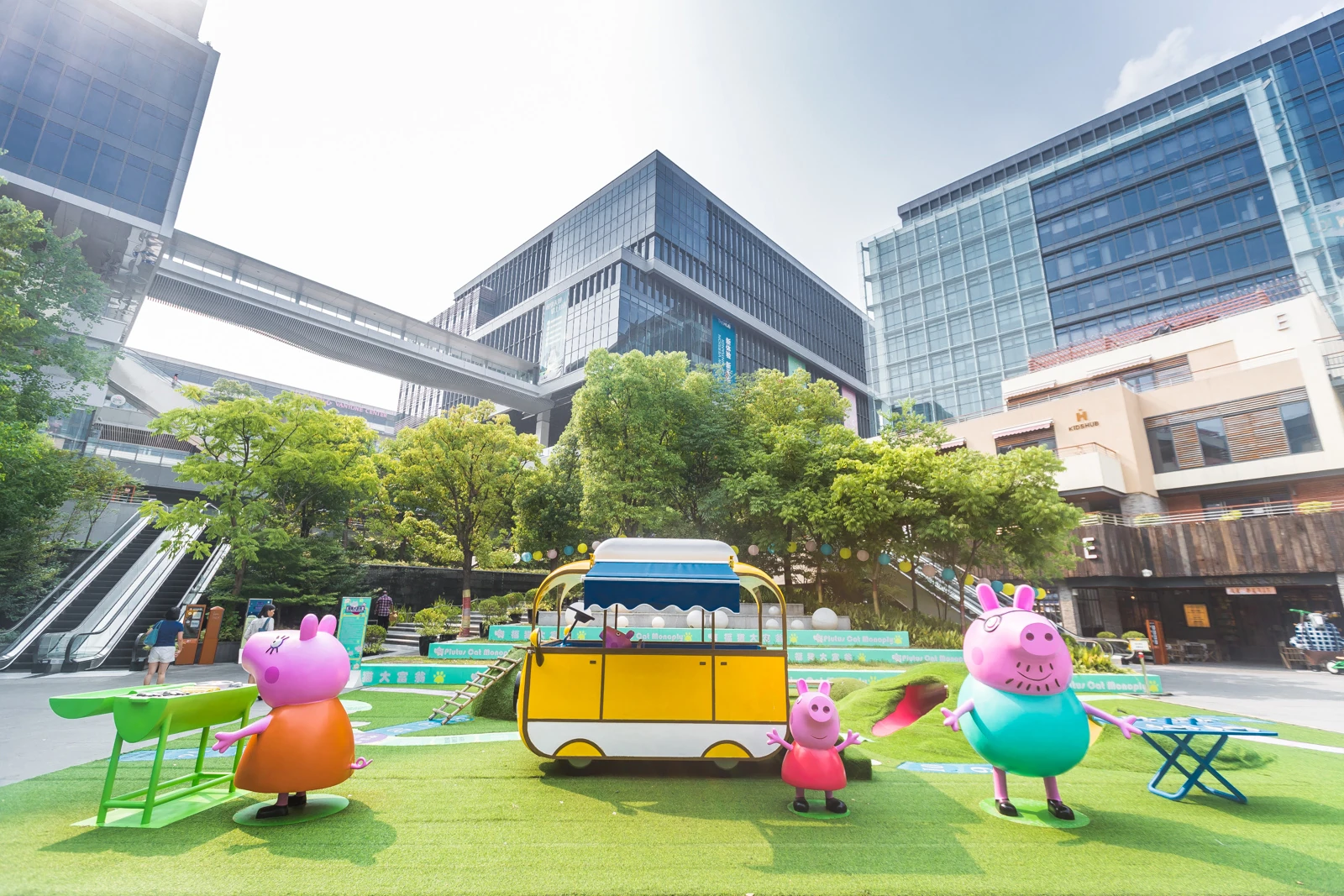 Peppa Pig and family characters around a yellow bus installation at The Hub